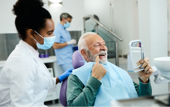 An image of a happy, smiling senior man completing routine preventative care while his hygienist looks on.